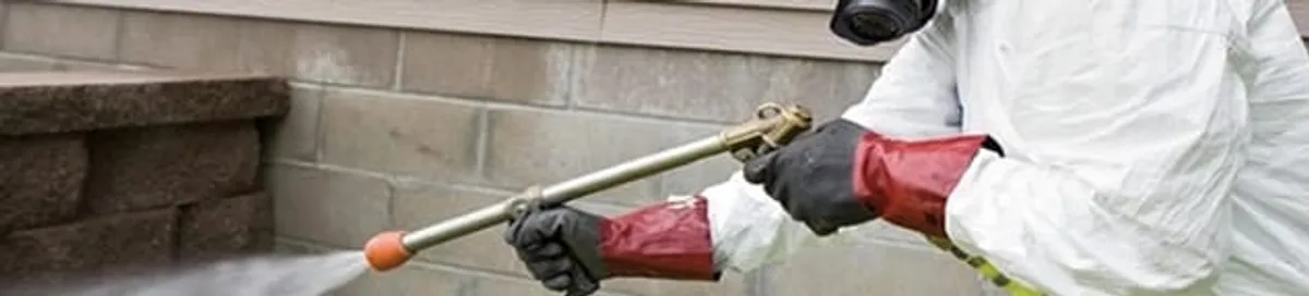 Pest control technician applying exterior insect treatment along a home foundation in Charlotte, NC