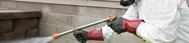 Pest control technician applying exterior insect treatment along a home foundation in Charlotte, NC