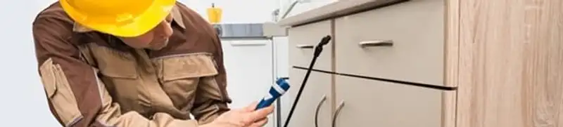 Roach exterminator applying treatment under kitchen cabinets in Charlotte, NC