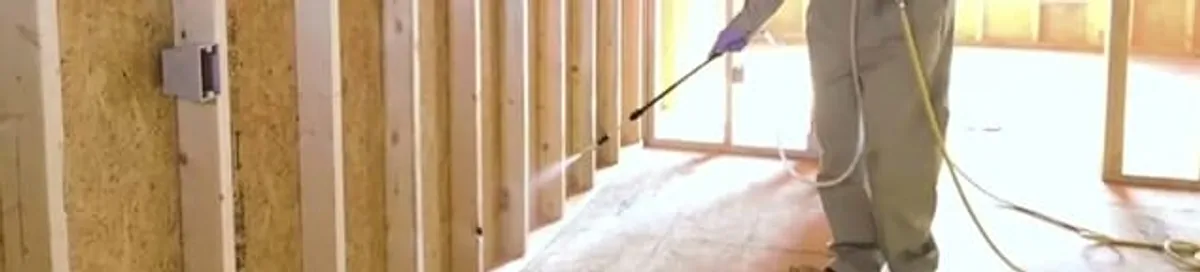 Termite treatment technician applying spray along framing and unfinished walls in Charlotte, NC