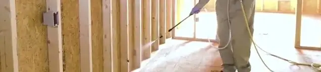 Termite treatment technician applying spray along framing and unfinished walls in Charlotte, NC